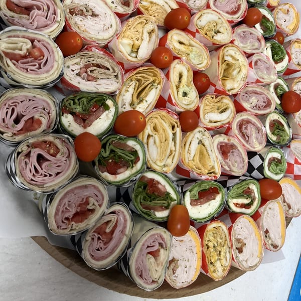 An assortment of Sub-Ology sandwich pinwheel wraps with various fillings and cherry tomatoes.