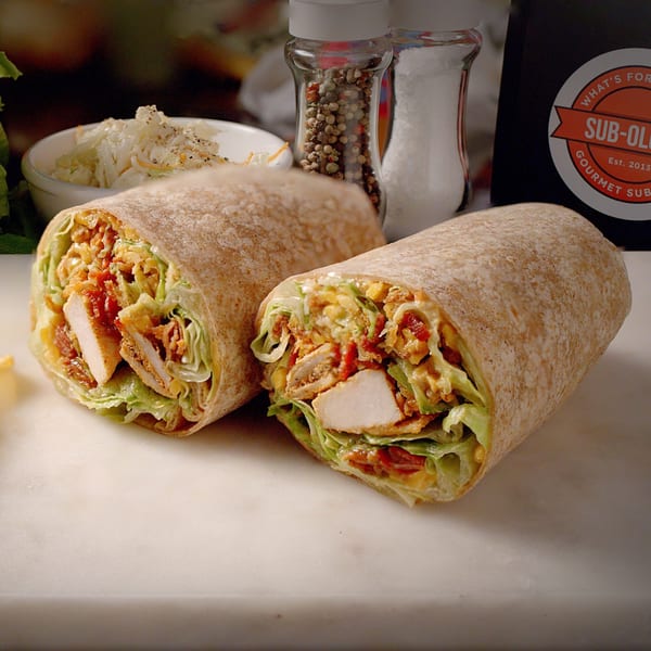 Two Sub-Ology chicken wraps with lettuce and sauce, a side of coleslaw, and salt and pepper shakers.