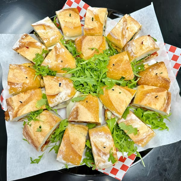 A catering platter of Sub-Ology's assorted sandwich halves, garnished with fresh arugula.