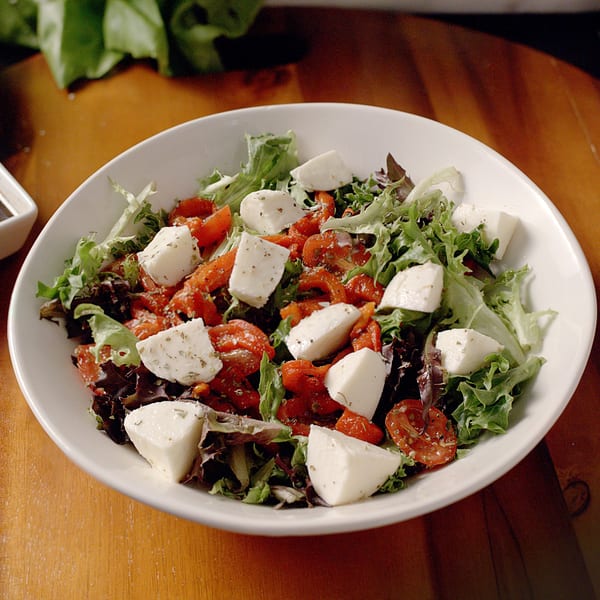 A fresh salad with mixed greens, cherry tomatoes, and mozzarella cheese in a white bowl.