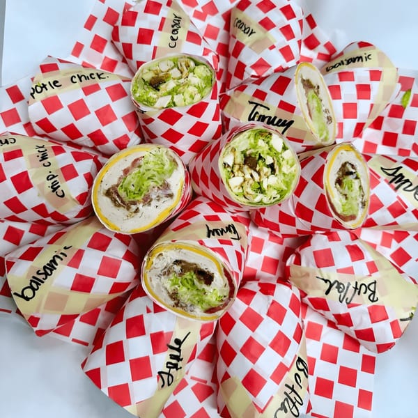 Assortment of Sub-Ology wraps, some open to show fillings, in red and white checkered paper.